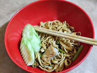 A bowl of chicken noodles with fresh cucumber slices, tofu pieces and celery sticks, served with...