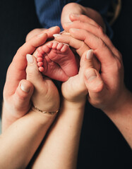 The babys feet remain at the center, surrounded by adult hands that gently cradle them. The natural skin tones and added warmth in the image enhance the feeling of tenderness, love, and family bonding