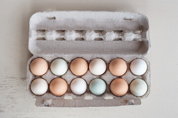 A rustic grey egg carton sits open on a light wooden surface, revealing a dozen farm-fresh eggs