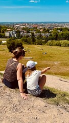 Mother and daughter sitting on hill with view on city of Cracow. Two people observe landscape among nature and park. Outdoors.