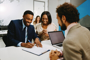 Couple  signing contract with insurance agent in modern office, happy and satisfied with the deal