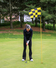 Woman Preparing to Putt on a Golf Course Surrounded by Trees