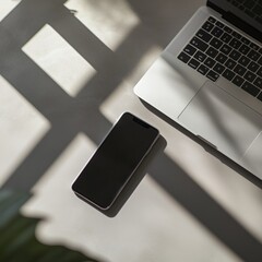 Smartphone and laptop on sunlit desk with shadows