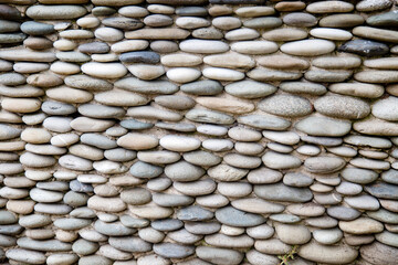 The wall is made of oval-shaped pebbles of gray color. Backgrounds, textures, design.