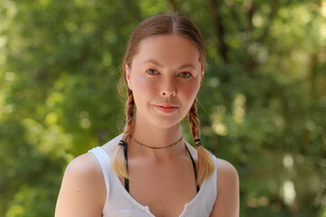Naklejka premium Front-facing portrait of calm woman with natural skin tone, minimal makeup, and subtle expression outdoors in summer lighting