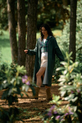 Curly-haired woman strolls through lush green forest in a fashionable raincoat