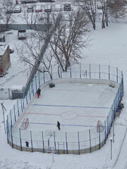 Hockey rink with a red and white line. There are two people playing hockey on the rink in yard