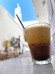 Closeup view of a Greek freddo espresso with rich crema, set against a softly blurred background of a picturesque Cycladic island, evoking summer vibes, relaxation, and Mediterranean charm.