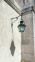 Aged lantern casts whimsical shadows on sunlit wall, evoking nostalgia of forgotten streets,...