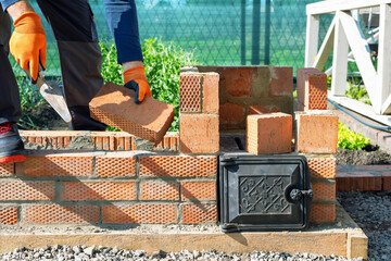 bricklayer building wood oven outdoors. man building bricks barbeque at the backyard.