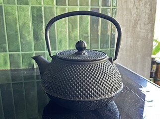 A black teapot with its handle raised sits on a stove