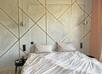 Bedroom interior, rumpled bed, two lamps above the bed, grey wall with gold stripes