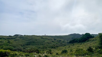 Enigmatic rolling hills cloak a hidden lighthouse, verdant sanctuary whispers of Beltane revelry and timeless Gaelic mystery