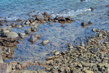 View of beach waves breaking on dark rocks during low tide. Paradise beach. Impeccable nature.