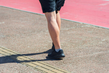 Lower part of an unidentified person walking on a street sidewalk during strong sunlight. Activity, direction,