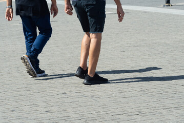 Half-body view of unidentified people walking down a street from a sidewalk. Pedestrians.