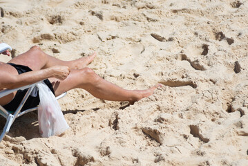 Unidentified person sitting on a beach chair sunbathing on the seashore during strong sunshine.