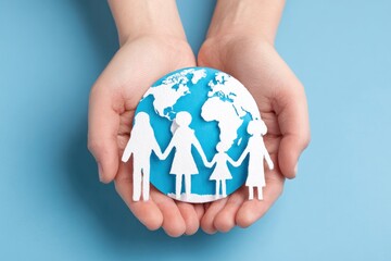 Two hands cradle a blue paper globe with white continents Four paper cutout figures resembling a family stand in front of the globe holding hands