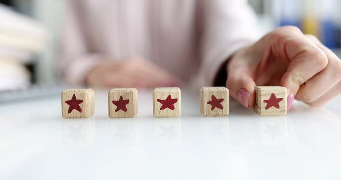 Office worker adds fifth wooden block with red star to four other blocks. Woman completes five star rating indicating excellent customer service