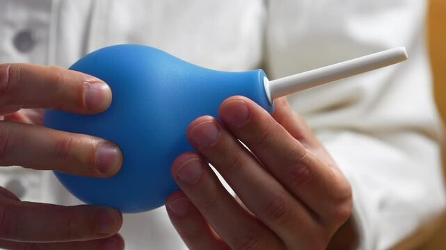 Blue enema in the hands of a doctor before use in a hospital.
Stomach and intestinal problems.
Treatment of constipation with an enema.
Topic of medicine