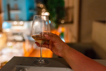 A woman's hand holds a glass of wine on the balcony ledge of a hotel in the summer evening, at night. Vacation time.