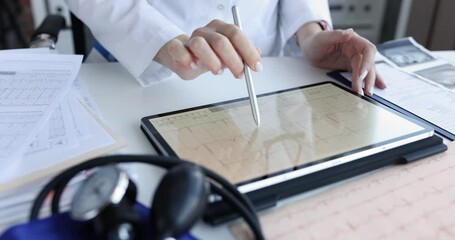 Professional reviews cardiac data on digital tablet pointing at electrocardiogram with stylus. Medical equipment highlights healthcare technology - Powered by Adobe