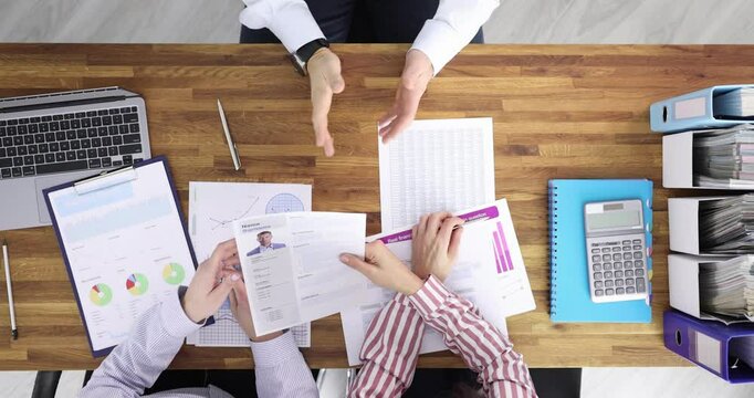 Job candidate shakes hands with hiring professionals and submits resume for office position. Job application process at desk in corporate setting