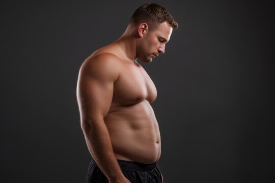 A muscular man, showing his belly and waistline after weight loss on a black background