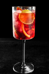 Refreshing red cocktail in a tall glass with ice cubes, lime and orange slices, set against a dark background. Ideal for summer, parties, or bar and beverage themes
