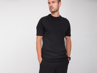 young stylish guy in black t-shirt and black pants is standing straight and looking away on the white wall background. medical concept. free space on left side, mockup
