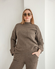 young stylish plus size blonde girl in brown casual costume is standing fashion and looking straight in sunglasses on the white art wall background. teen fashion. fashion concept, free space