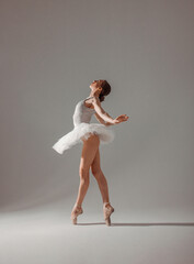 young slim dancer, fit girl ballerina stands in white ballet tutu like white swan in profile in pointe shoes on white wall background in studio light. classic ballet posing. ballet concept, free space