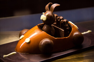 The chocolate rabbit rides in a chocolate car with chocolate bunnies. the cake is in the shop window behind the glass. confectionery concept, free space