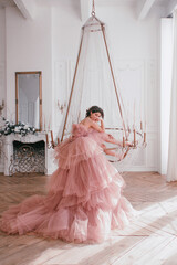 young girl with short black hair in pink princess dress is sitting on the huge crystal chandelier...