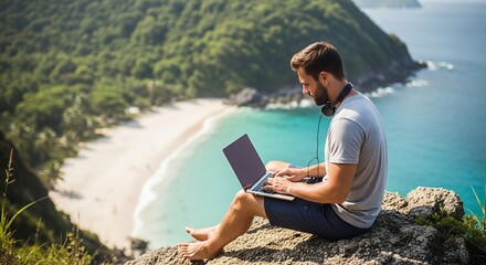 Bearded Man Using Laptop on Rocky Cliff Overlooking Tropical Beach