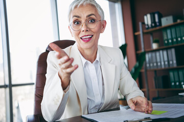 Successful mature businesswoman with short white hair smiling while working at her modern office desk