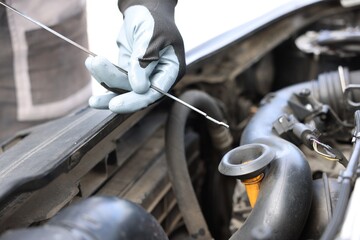Worker checking motor oil level in car with dipstick, closeup