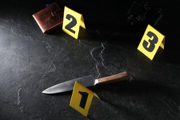 Forensic expert. Yellow evidence markers, knife and wallet on black table, above view