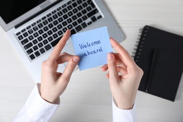 Woman holding paper note with words Welcome Aboard at light wooden table, top view