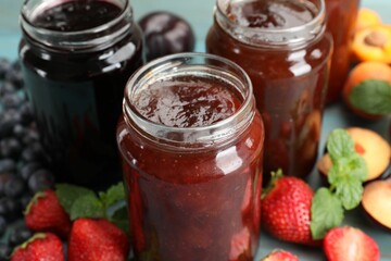 Different jams in jars and ingredients on blue wooden table, closeup
