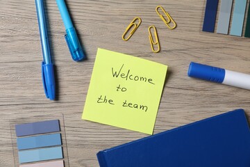Paper note with phrase Welcome To The Team and stationery on wooden table, flat lay