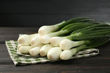 Fresh ripe green onions and towel on black wooden table, closeup
