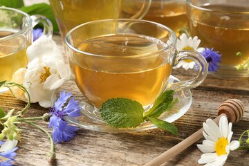 Aromatic herbal tea in glass cups, mint and flowers on wooden table, closeup
