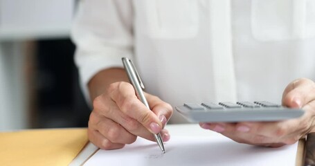 Businesswoman calculates and writes detailed financial report with calculator and pen. Essential accounting and bookkeeping tasks in office setting