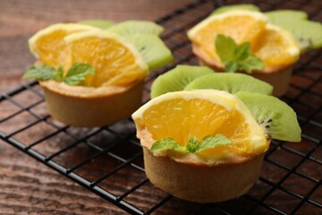 Tartlets with fruits and mint on wooden table, closeup. Delicious dessert