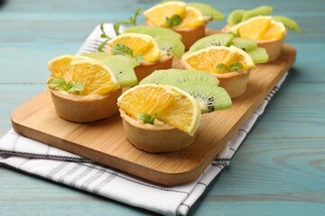 Tartlets with fruits and mint on light blue wooden table, closeup. Delicious dessert