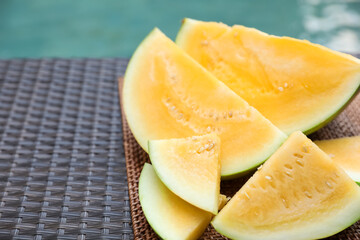Pieces of ripe yellow watermelon on wicker table near swimming pool, closeup. Space for text