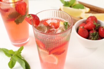 Refreshing drink with strawberries, mint, lemon and ice on white table, closeup