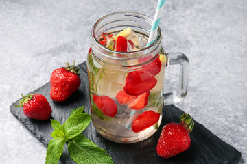 Refreshing drink with strawberries, lemon, ice and mint on grey textured table, closeup