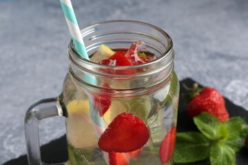 Refreshing drink with strawberries, ice and mint on grey textured table, closeup